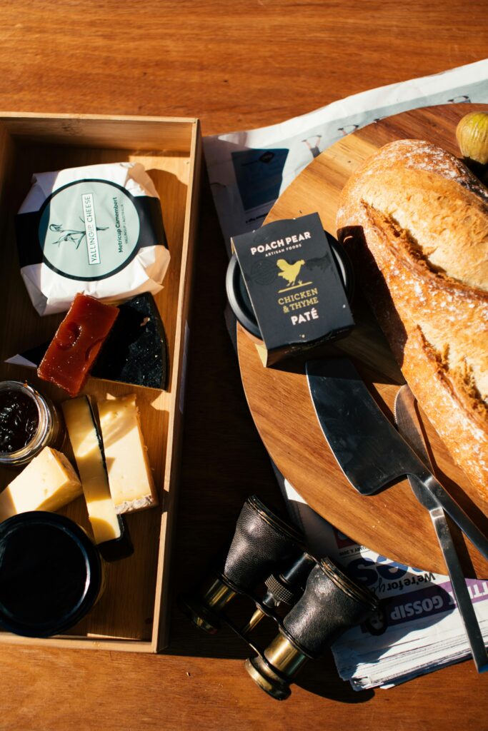 Top view of tasty loaf of bread with package of chicken pate on wooden tray on table with binocular and open box with stuff